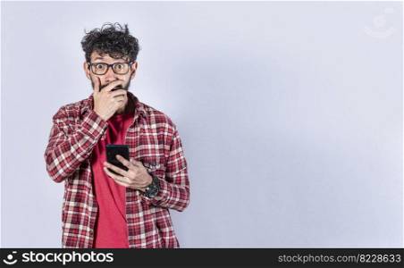 Man holding his cell phone and covering his mouth. surprised man receiving news on his cell phone isolated. Astonished man holding his cellphone and covering his mouth isolated