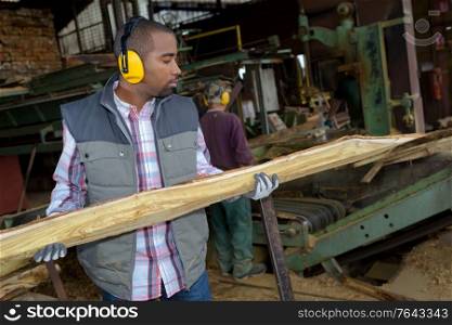 Man holding length of wood in saw mill