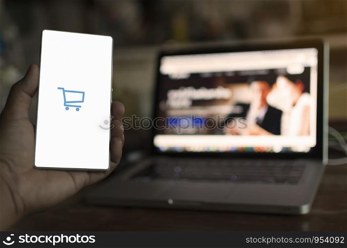 man holding mobile phone with app shopping online and laptop modeled from office tablet