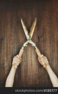 Man holding old manual hedge trimmer in front of wooden background.