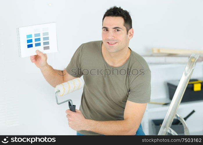 man holding paintbrush and color swatch in an apartment