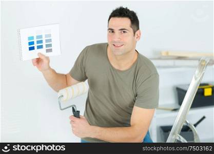 man holding paintbrush and color swatch in an apartment