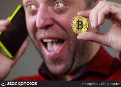 Man holding phone and crypto currency symbol. Adult guy using his smartphone calling to somebody having bitcoin.. Man talking on phone holding bitcoin