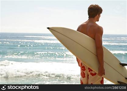 Man holding surfboard by ocean back view