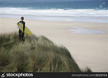 Man holding surfboard on cliff, looking at sea, back view