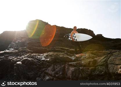 Man holding surfboard on large rocks