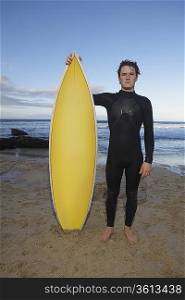 Man holding surfboard standing on beach, portrait