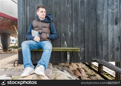 Man holding tablet pc sitting on a bench in front of wooden wall