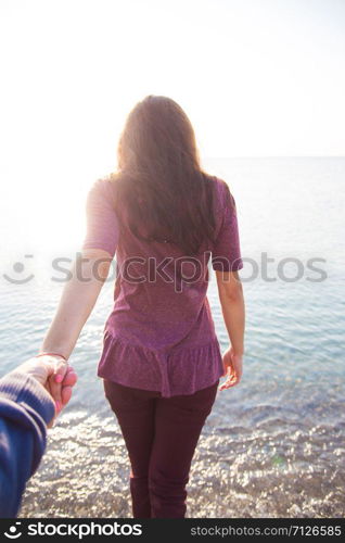 man holding the hand of a girl who stands with his back to the sea. man holding the hand of a girl who stands with his back to sea