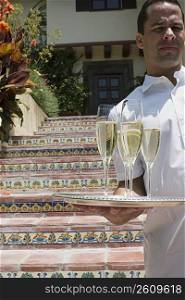 Man holding tray of champagne in front of outdoor stairs