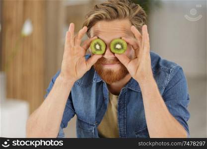 man holding two sliced kiwis on his eyes