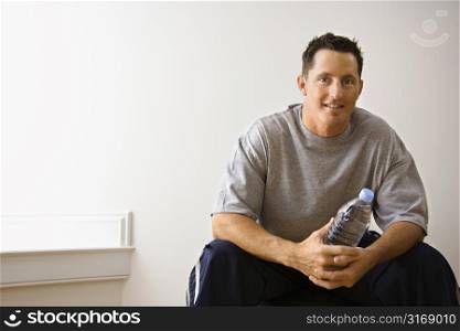 Man holding water bottle sitting on balance ball at gym smiling.