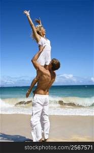 Man holding woman up in air on Maui, Hawaii beach.