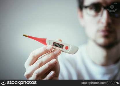 Man holds a red fever thermometer with high temperature in his hand, blurry face