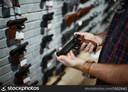 Man holds handgun in gun shop. Male person buying pistol for security in weapon store, selfdefence and sport shooting hobby. Man holds handgun in gun shop