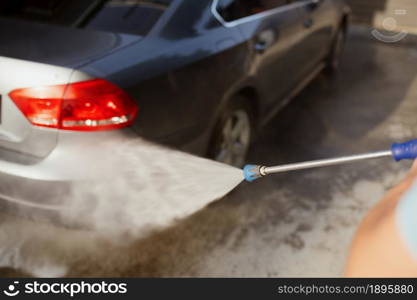 Man holds high pressure water gun, car wash station. Carwash industry or business. Male person cleans his vehicle from dirt outdoors. Man holds high pressure water gun, car wash