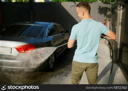Man holds high pressure water gun, car wash station. Carwash industry or business. Male person cleans his vehicle. Man holds high pressure water gun, car wash