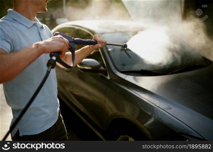 Man holds high pressure water gun, hand car wash station. Car-wash industry or business. Male person cleans his vehicle from dirt outdoors. Man holds high pressure water gun, hand car wash