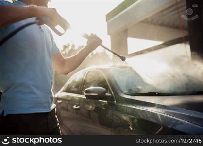 Man holds high pressure water gun, hand car wash station. Car-wash industry or business. Male person cleans his vehicle from dirt outdoors. Man holds high pressure water gun, hand car wash