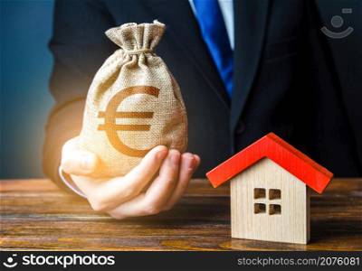 Man holds out a euro bag near the house. Bank approval for issuing a mortgage loan. Home purchase, invest in real estate. Property appraisal. Favorable terms and conditions, low interest rate.