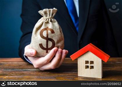 Man holds out a money bag near the house. Bank approval for issuing a mortgage loan. Favorable terms and conditions, low interest rate. Home purchase, invest in real estate. Property appraisal.