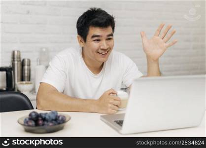 man home during pandemic having video call laptop waving