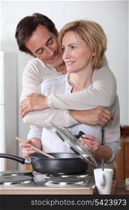 Man hugging a woman cooking at an electric stove