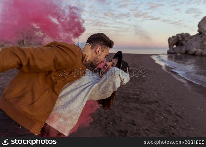 man hugging woman with pink smoke bomb sea shore