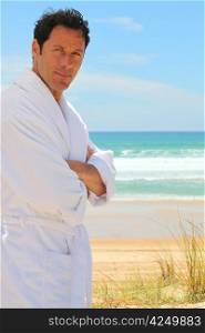 Man in a bathrobe standing on a sandy beach