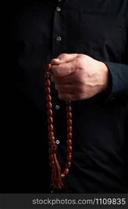 man in a black shirt holds a brown stone rosary in his left hand, low key. used to count prayers or other ritual actions, to preserve attention and concentration, to set the rhythm