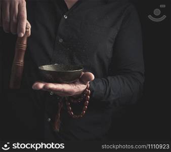 man in a black shirt rotates a wooden stick around a copper Tibetan bowl of water. ritual of meditation, prayers and immersion in a trance. Alternative treatment