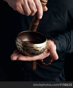 man in a black shirt rotates a wooden stick around a copper Tibetan bowl. ritual of meditation, prayers and immersion in a trance. Alternative treatment