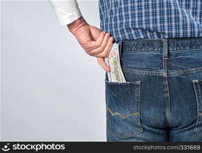 man in a blue plaid shirt and jeans puts paper American dollars in his back pocket, white background, copy space