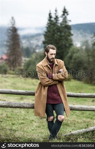 man in a brown coat and torn trousers was leaning against the fence