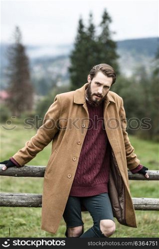 man in a brown coat and torn trousers was leaning against the fence