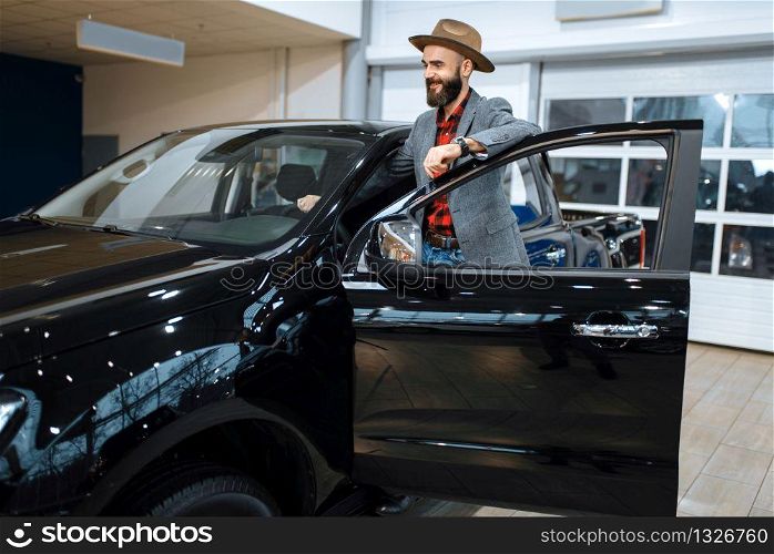 Man in a cowboy hat choosing new automobile in car dealership. Customer in vehicle showroom, male person buying transport, auto dealer business. Man in a cowboy hat, car dealership