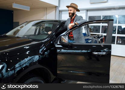 Man in a cowboy hat choosing new automobile in car dealership. Customer in vehicle showroom, male person buying transport, auto dealer business. Man in a cowboy hat, car dealership