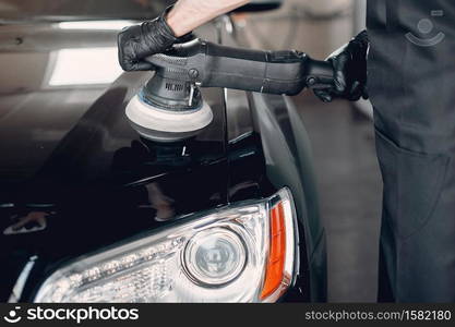 Man in a garage. Worker polish a car.