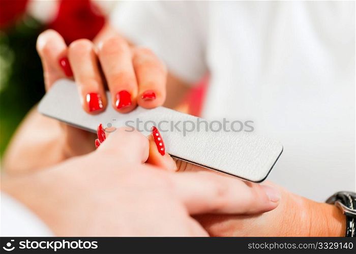 Man in a nail salon receiving a manicure by a beautician, lots of roses in the background