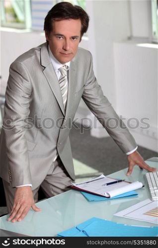 Man in a silver-grey suit purposefully standing by his desk