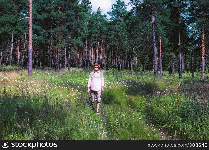 Man in a straw hat walking in pine forest and enjoying sunny summer day in the countryside. Vintage Film filter.. Man Walking in Pine Forest
