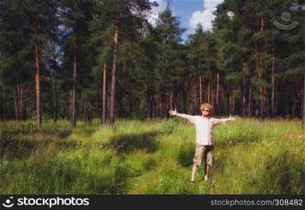 Man in a straw hat with arms raised standing in the pine forest and enjoying sunny summer day. Soft Film filter.. Man Raised Arms in Summer Forest
