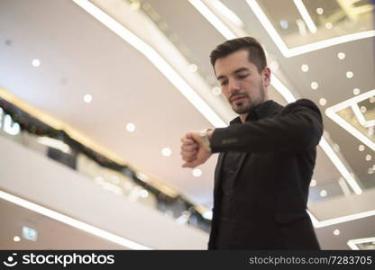 man in a suit indoors looks at his watch.