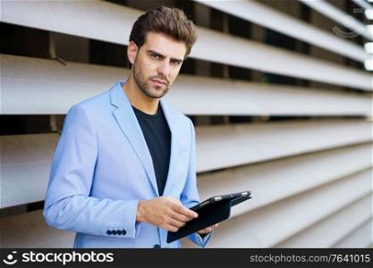 Man in a suit using a digital tablet outdoors. Businessman using a digital tablet near an office building