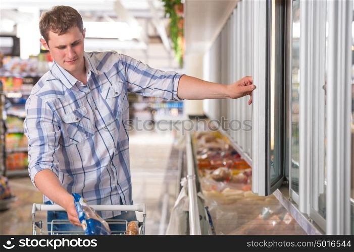 Man in a supermarket standing in front of the freezer looking for his favorite frozen food
