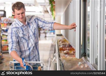 Man in a supermarket standing in front of the freezer looking for his favorite frozen food
