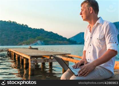 man in a white shirt with a laptop on the pier to meet a dawn