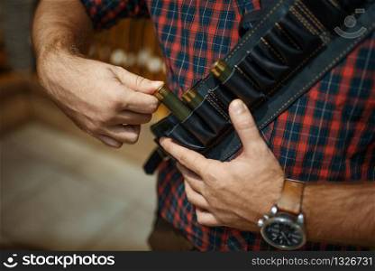 Man in ammo belt, rifles on background, gun shop. Euqipment for hunters on stand in weapon store, sport shooting hobby. Man in ammo belt, rifles on background, gun shop