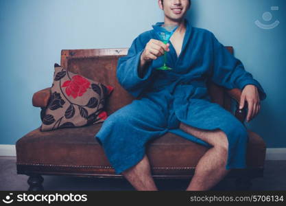 Man in bathrobe sitting on sofa and drinking cocktail