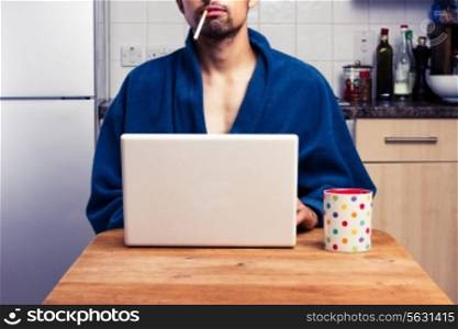 Man in bathrobe smoking and drinking while looking at laptop